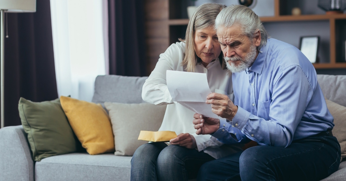 frustrated senior couple sitting on couch at home reviewing bills and taxes