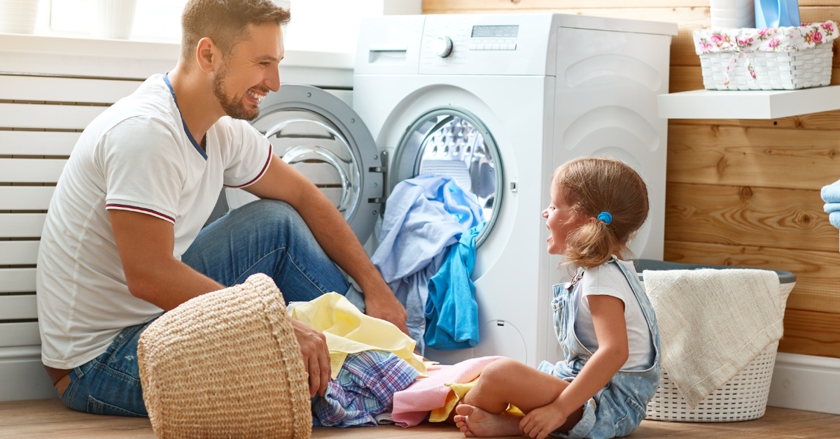 happy father and daughter sitting on floor doing laundry at home