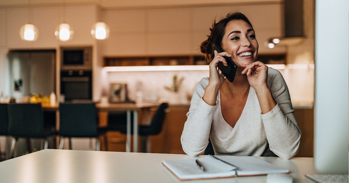 happy woman sitting on kitchen countertop talking on smartphone