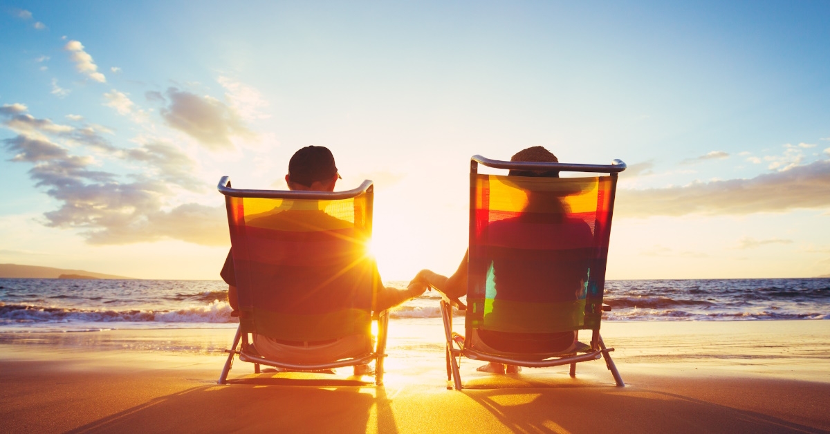 senior couple sitting on chairs at beach watching sunset