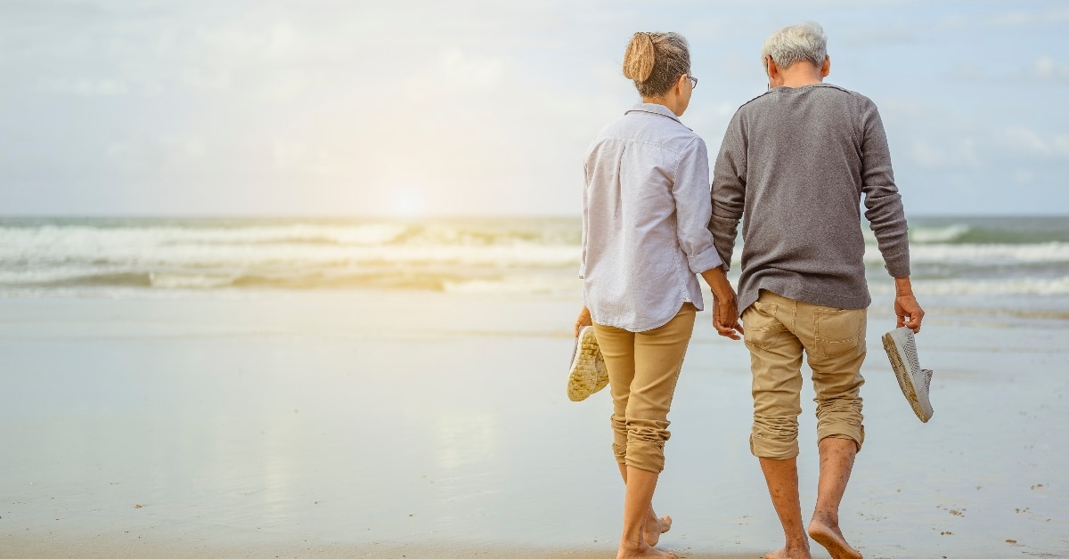 senior couple walking on the beach holding hands at sunrise,