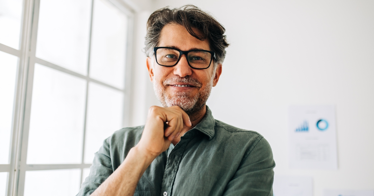 senior businessman stands in an office looking at the camera