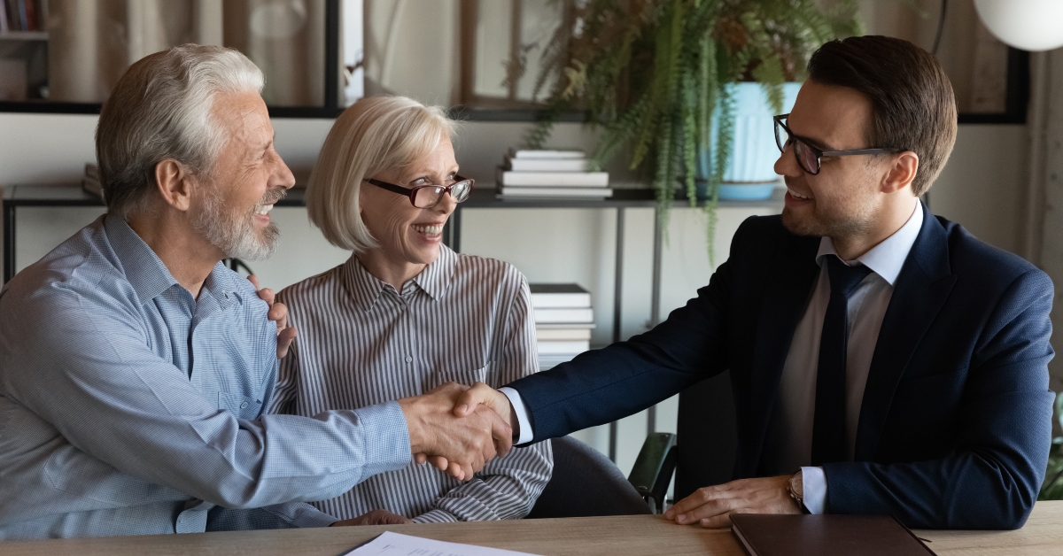 young man real estate broker handshaking with older family couple
