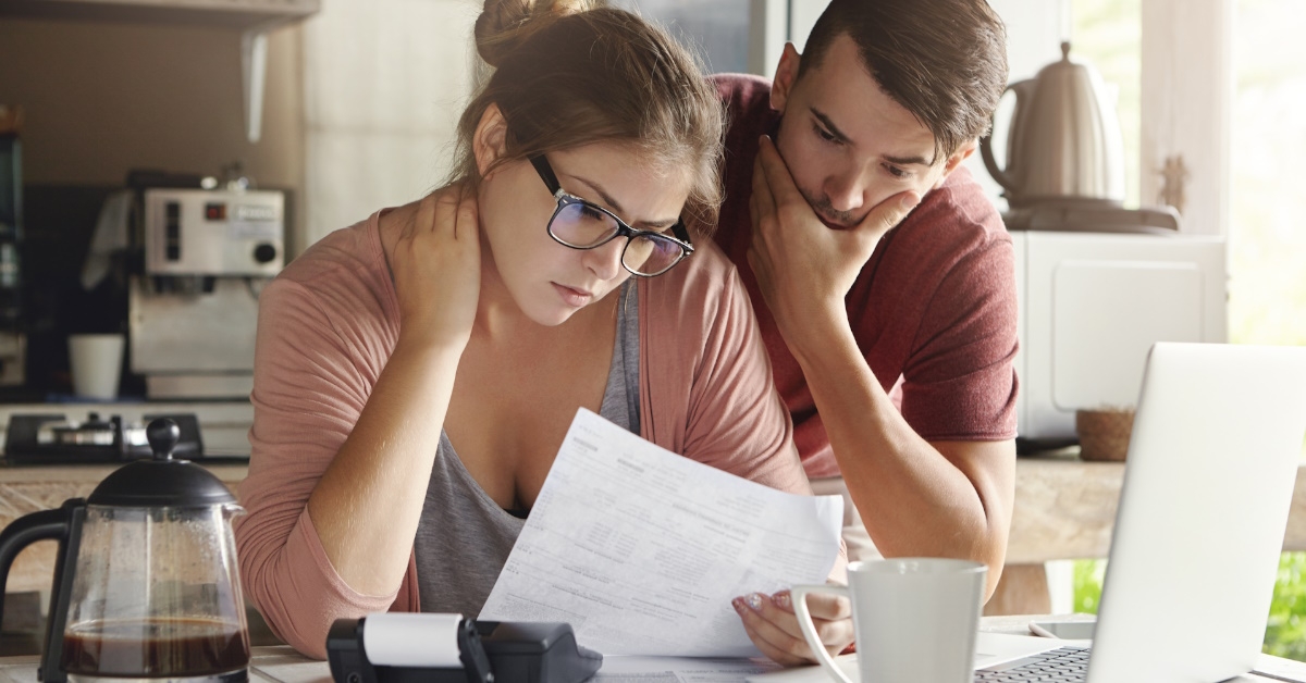 couple stressed while reviewing bills in home kitchen with coffee on table