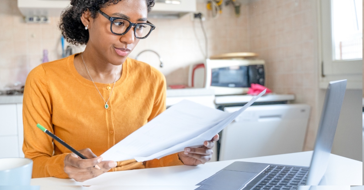 african american woman working from home sitting in kitchen reviewing papers 