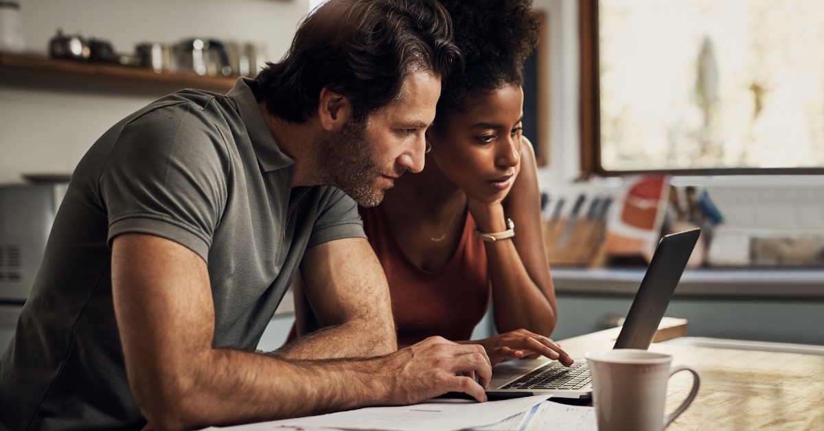 couple sitting together using laptop to check out budget at kitchen counter top