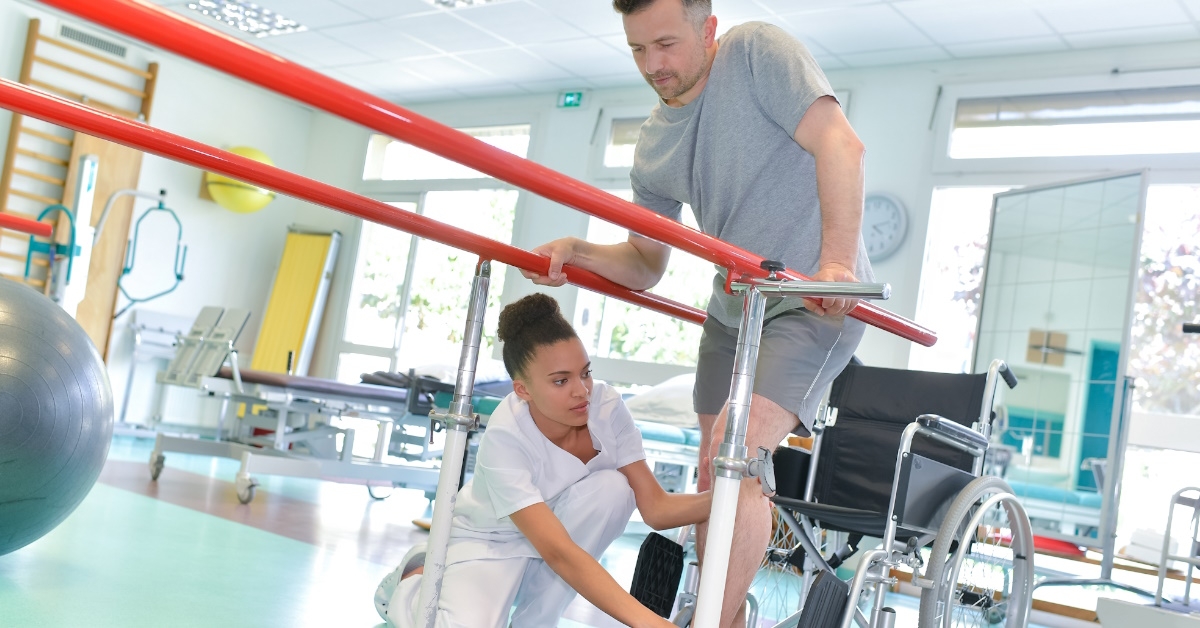 female therapist at clinic helping male patient to walk on track