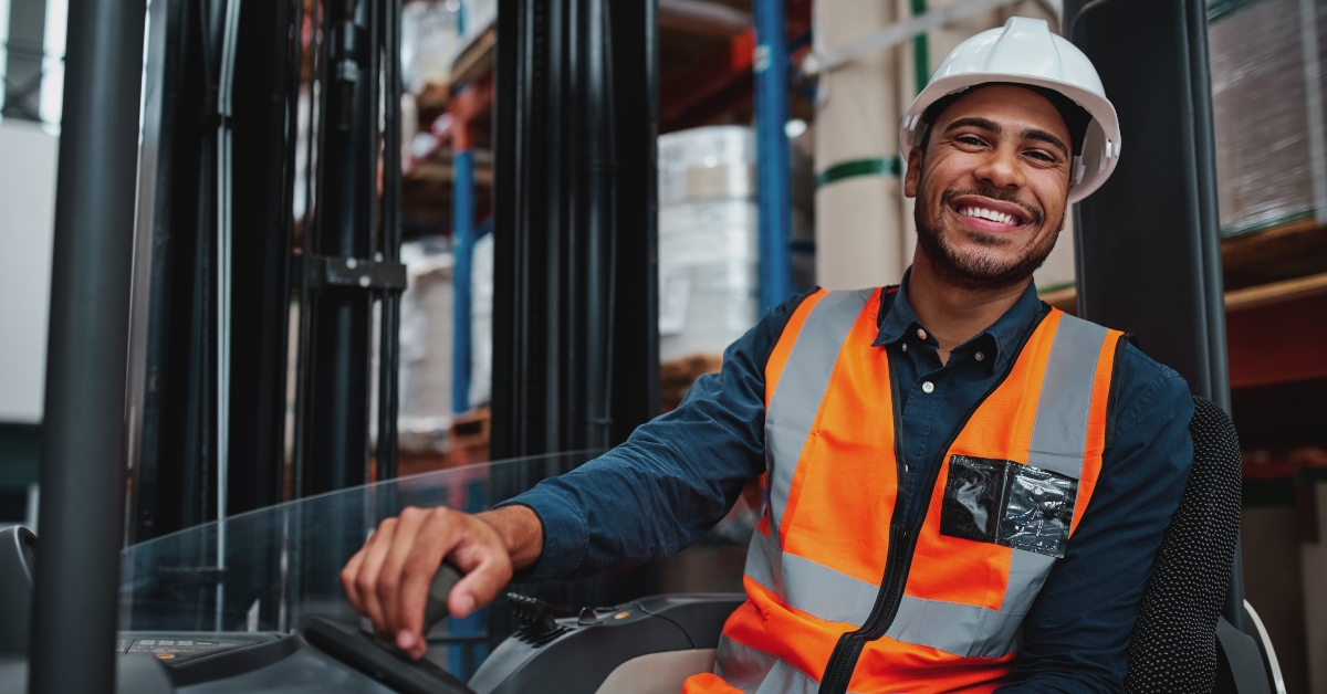 forklift driver sitting in vehicle in warehouse smiling