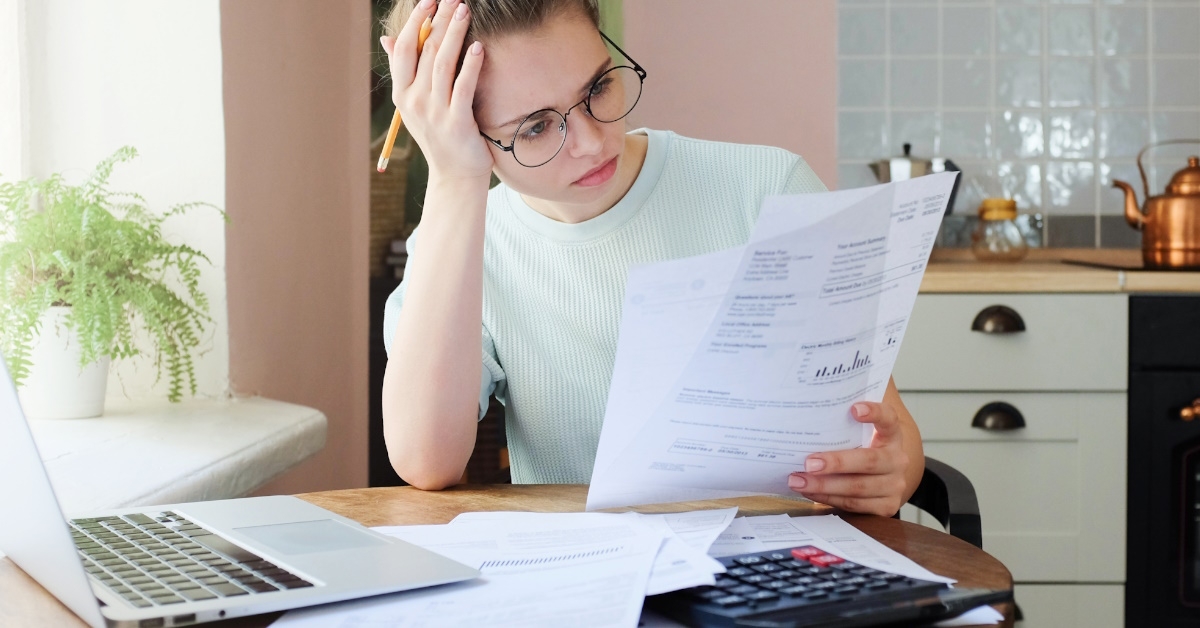 woman sitting at table with laptop stressing at bills in hand