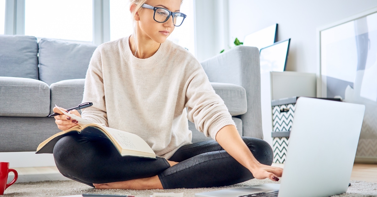 woman sitting on floor sorting out bills using laptop at home