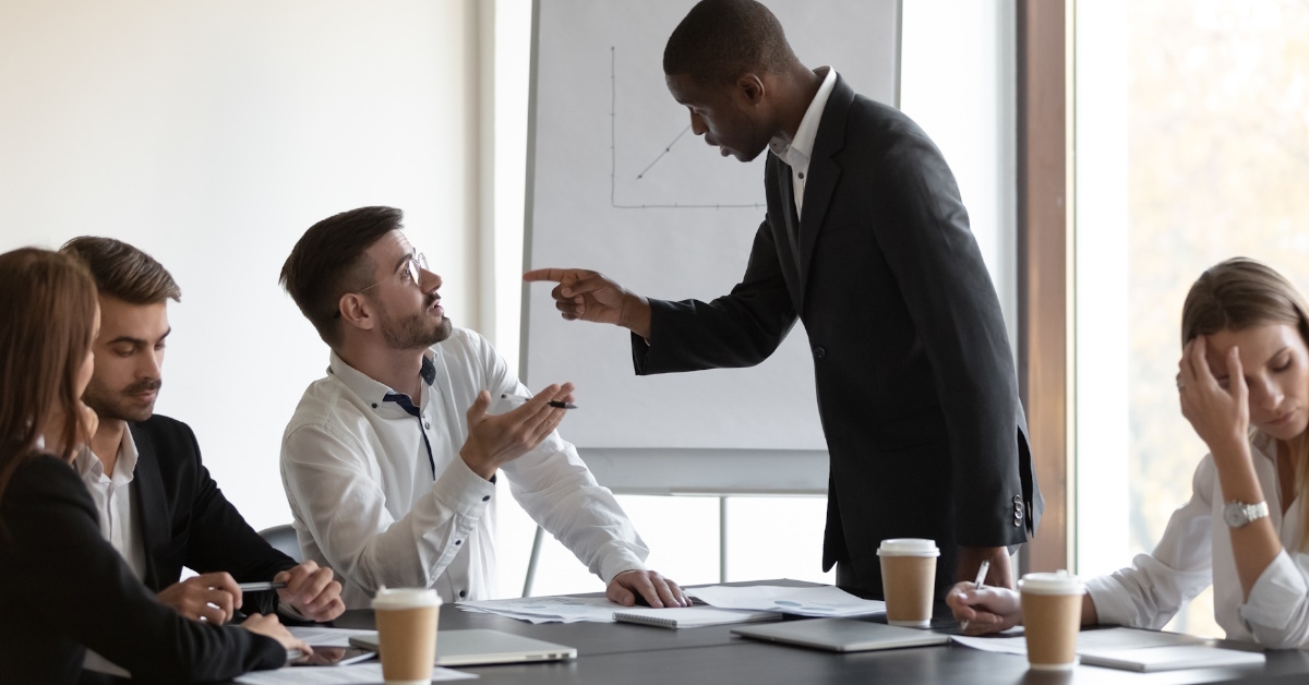 multi ethnic employees having argument at work with colleagues sitting at table