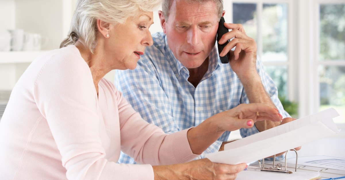 senior couple reviewing bills after retirement while talking on phone at home