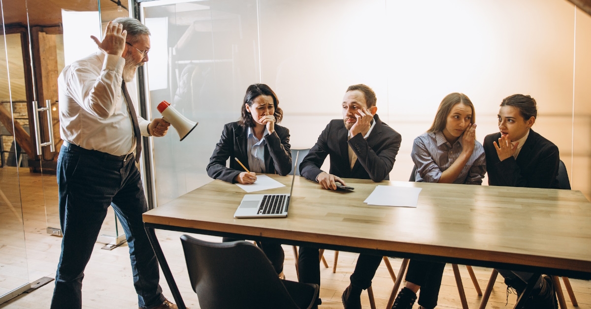 senior male boss holding megaphone and screaming over colleagues