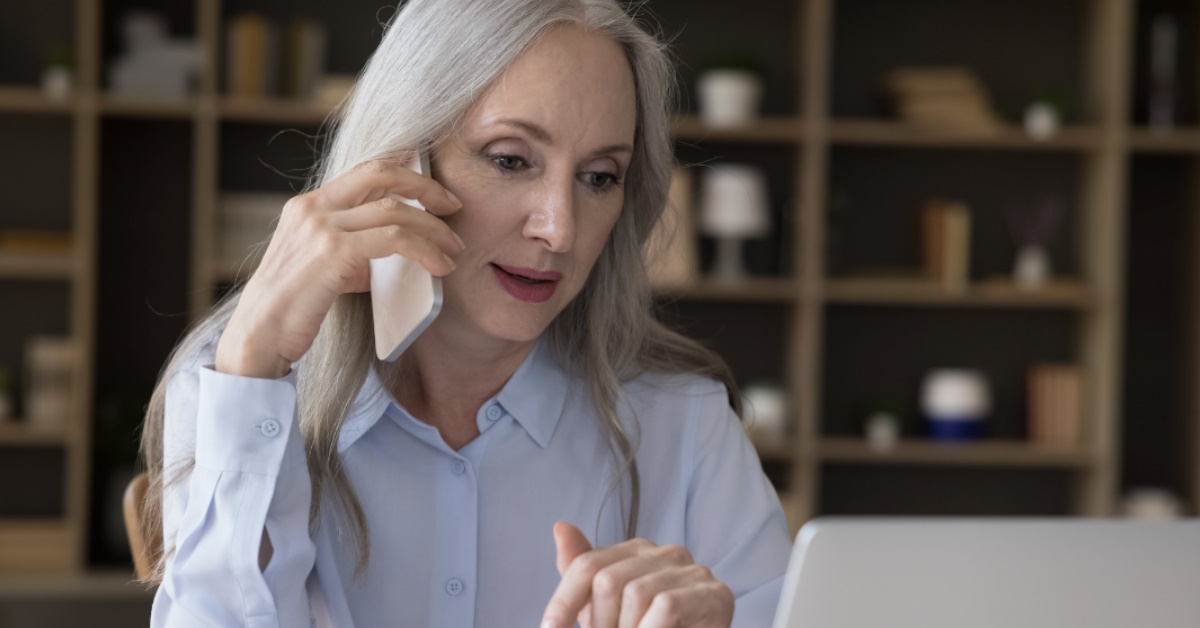 senior woman using laptop to work from home while talking on cellphone