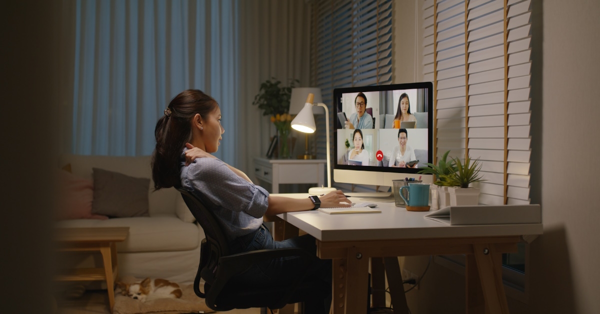 asian woman working from home on a desktop computer, relieving a stiff neck while having a video call with colleagues