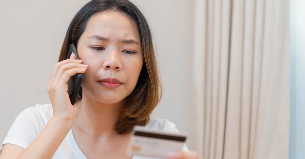 unhappy woman talking on phone while holding bank card in hand