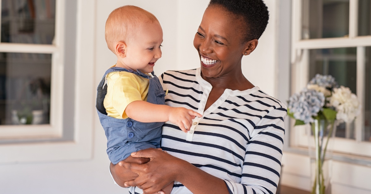 happy african american woman holding baby boy in arms at home