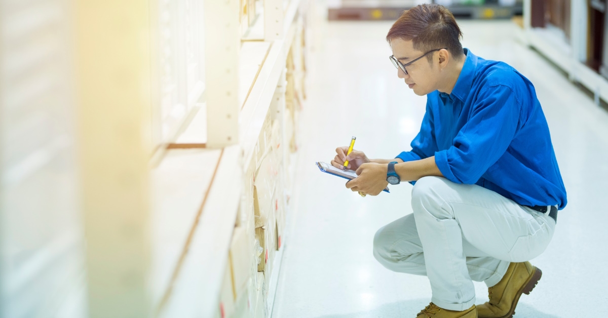 asian man seated on the warehouse floor, examining products using a digital pen and tablet.