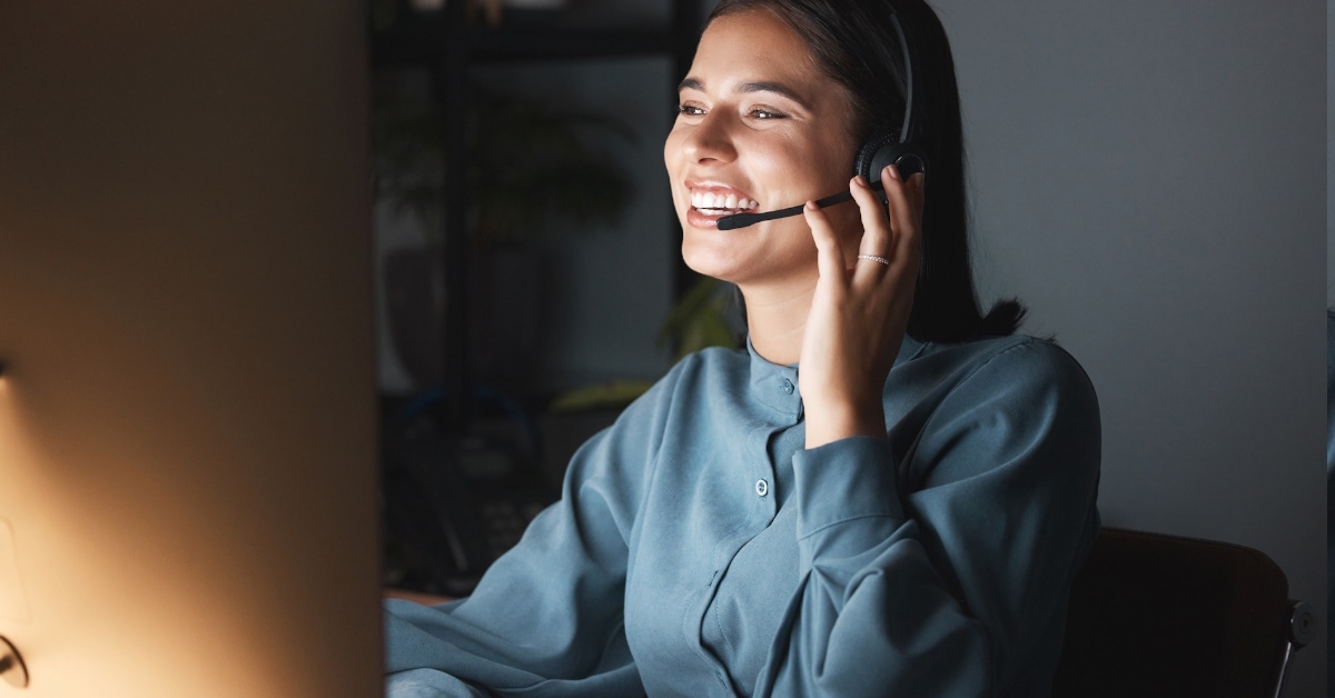 customer service woman wearing headset talking to client happily while using desktop computer