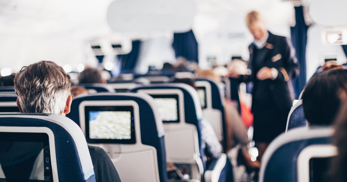 passengers sitting in airplane with stewardess standing in background