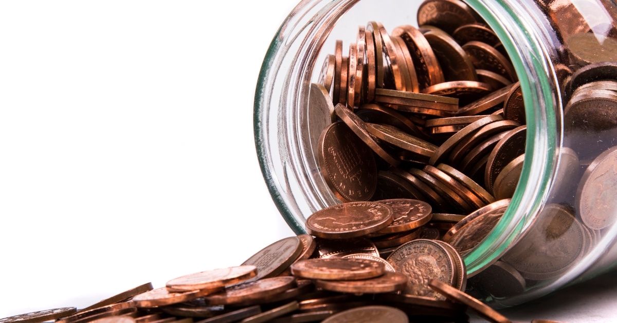 pile of british pennies spilling out of glass jar on white table