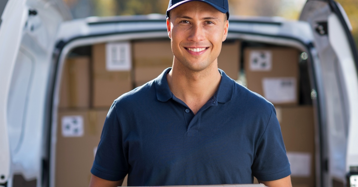 delivery man with a box, standing next to a van filled with more boxes