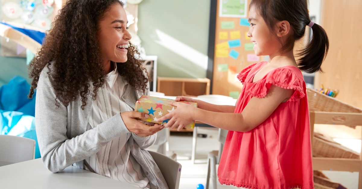 kindergarten teacher receiving gift from girl in classroom