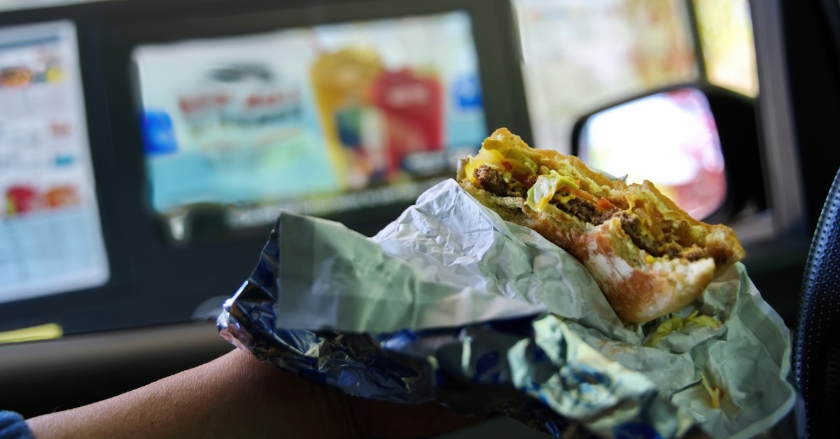 holding half eaten cheeseburger in hand while parking car