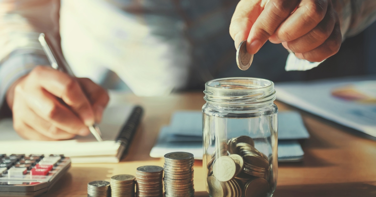 man writing on notepad while saving pennies in mason jar
