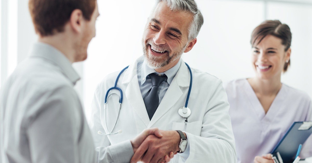 patient shaking hand with senior doctor at clinic with female nurse in background