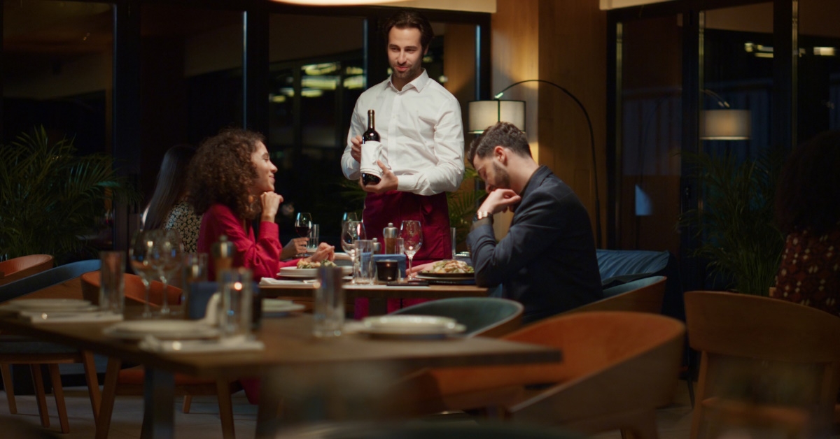 waiter popping bottle of champagne for couple in fancy restaurant 