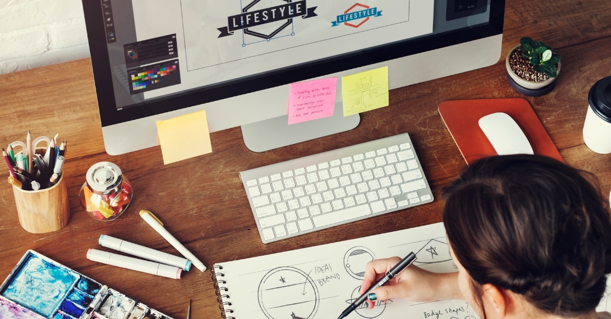 Female artist making designs on a paper while working in studio with color,pens,brush and paints on the table.