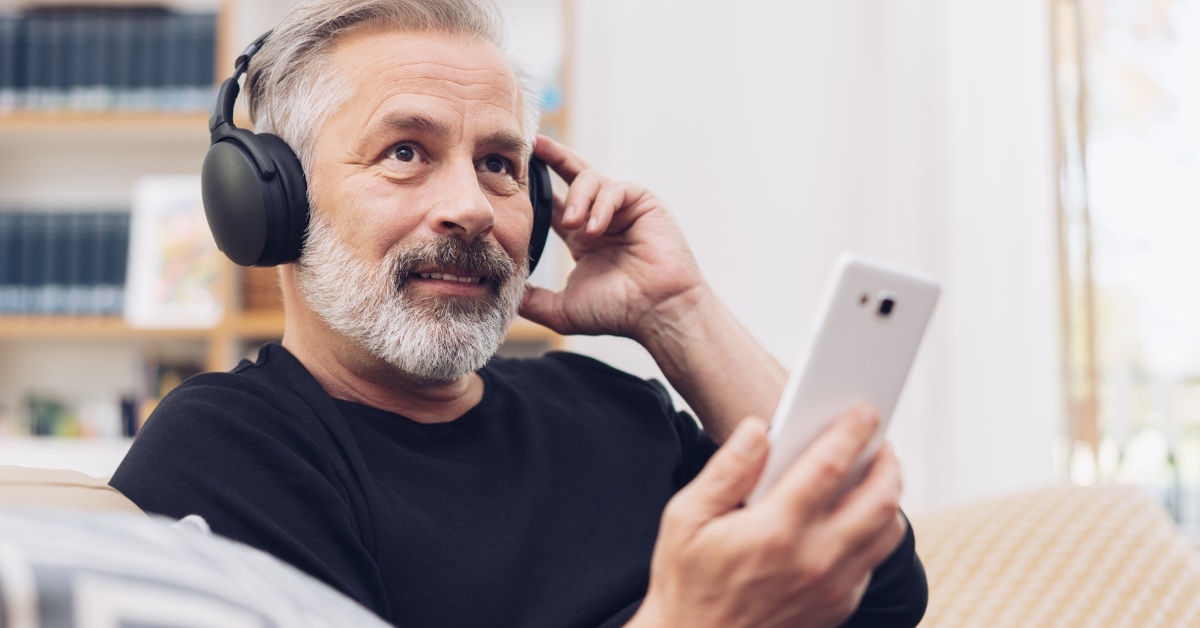 Middle-aged man wearing headphones listening to music online at home