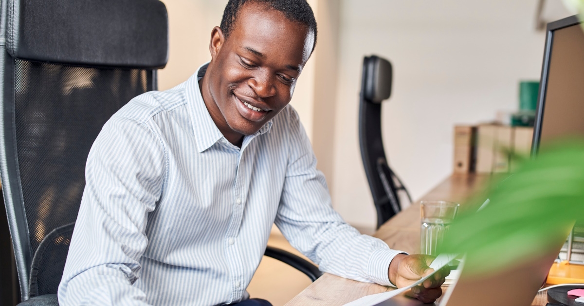 Smiling young african bussinessman calculating business income on calculator doing paperwork in office