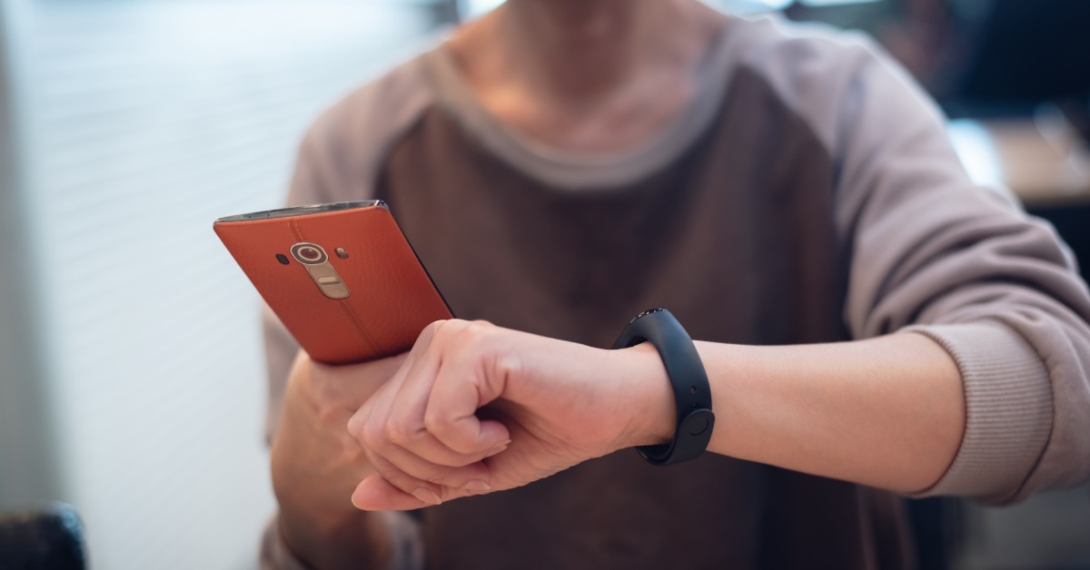 woman wearing T-shirt islooking at her smart watch while holding mobile in other hand