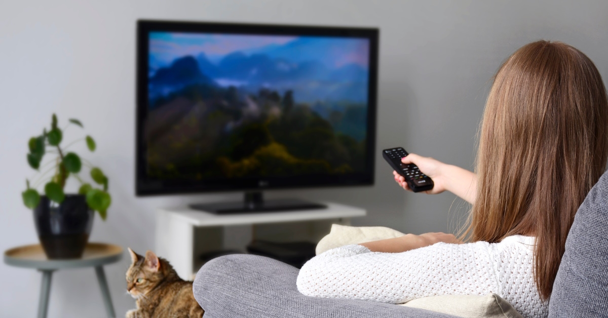 A young woman watching a nature documentry on TV while sitting with her cat on sofa in living room at home.
