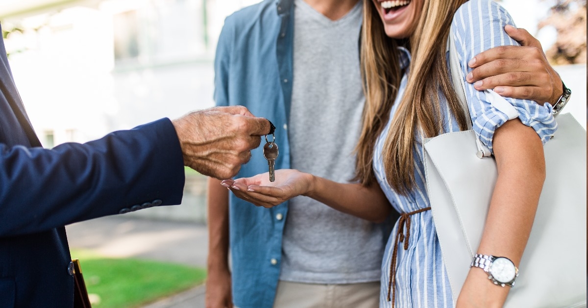 young happy couple receiving keys of new house from real estate agent