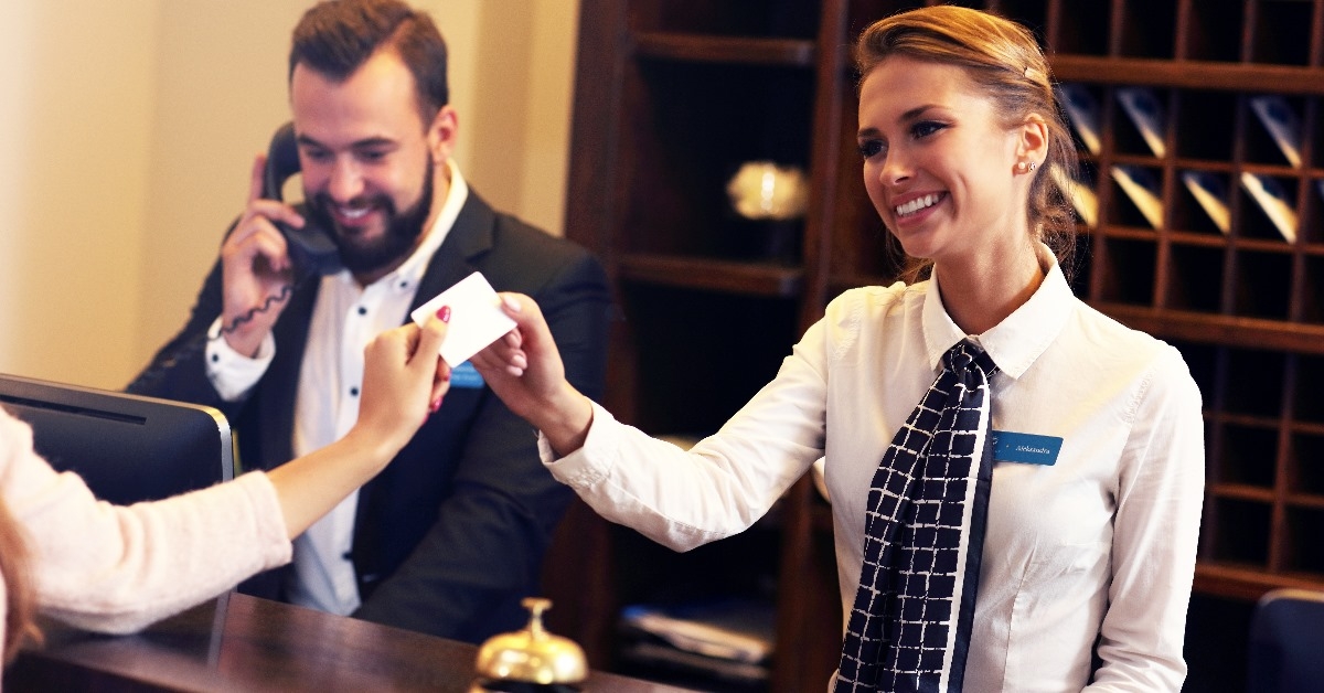 guest receiving keycard in hotel from female receptionist with male receptionist in background