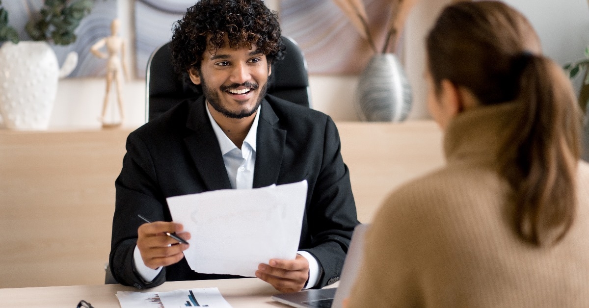 cheerful male manager interviewing female candidate at work while holding cv