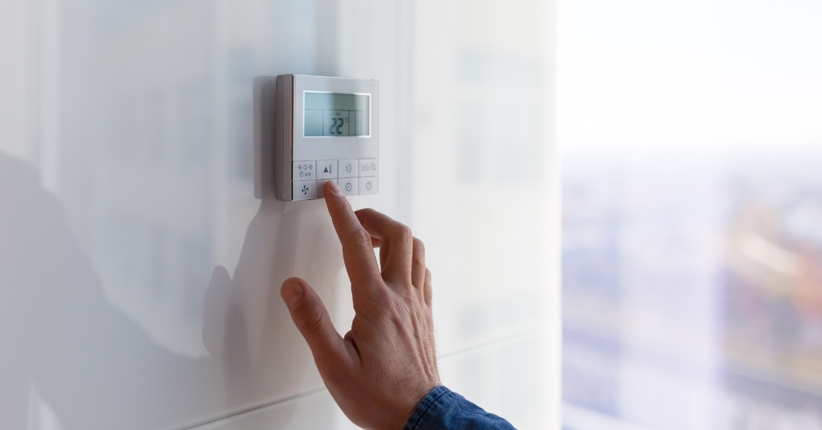 man controlling thermostat system on wall in apartment