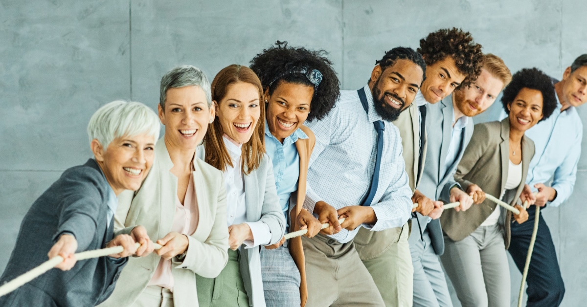 multi ethnic employees of different age group pulling rope to show concept of teamwork at office