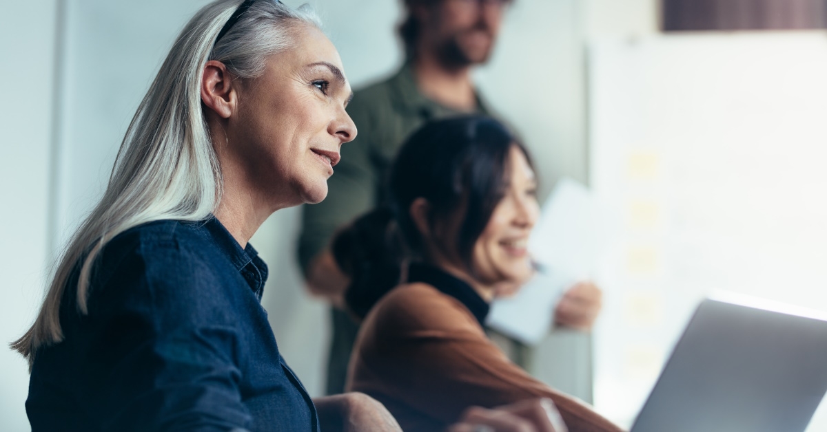 senior business woman sitting with colleagues using laptop for presentation at office