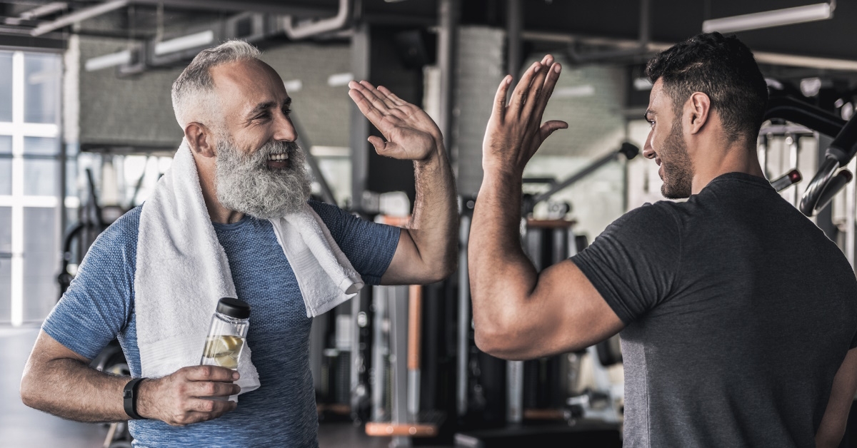 In a modern gym, a happy father and son chat and celebrate with a high five after workout.