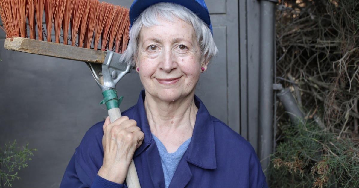  A senior woman is standing with a broom, working as a street cleaner.