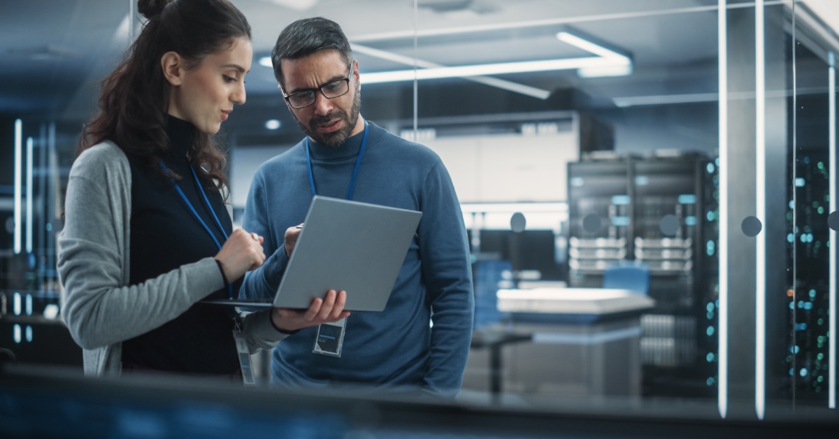 Male and female engineers discuss Artificial intelligence software on laptop and chat casually in a high-tech research office.