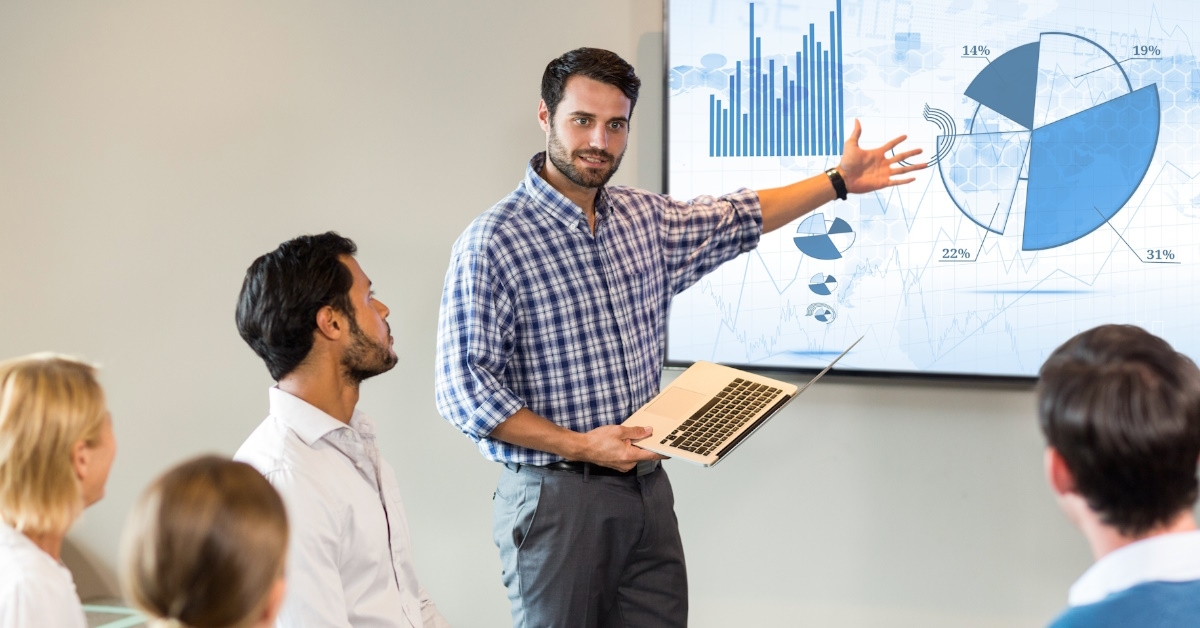 A male employee wearing a checkered shirt is explaining statistical data related to the business during a presentation at office.