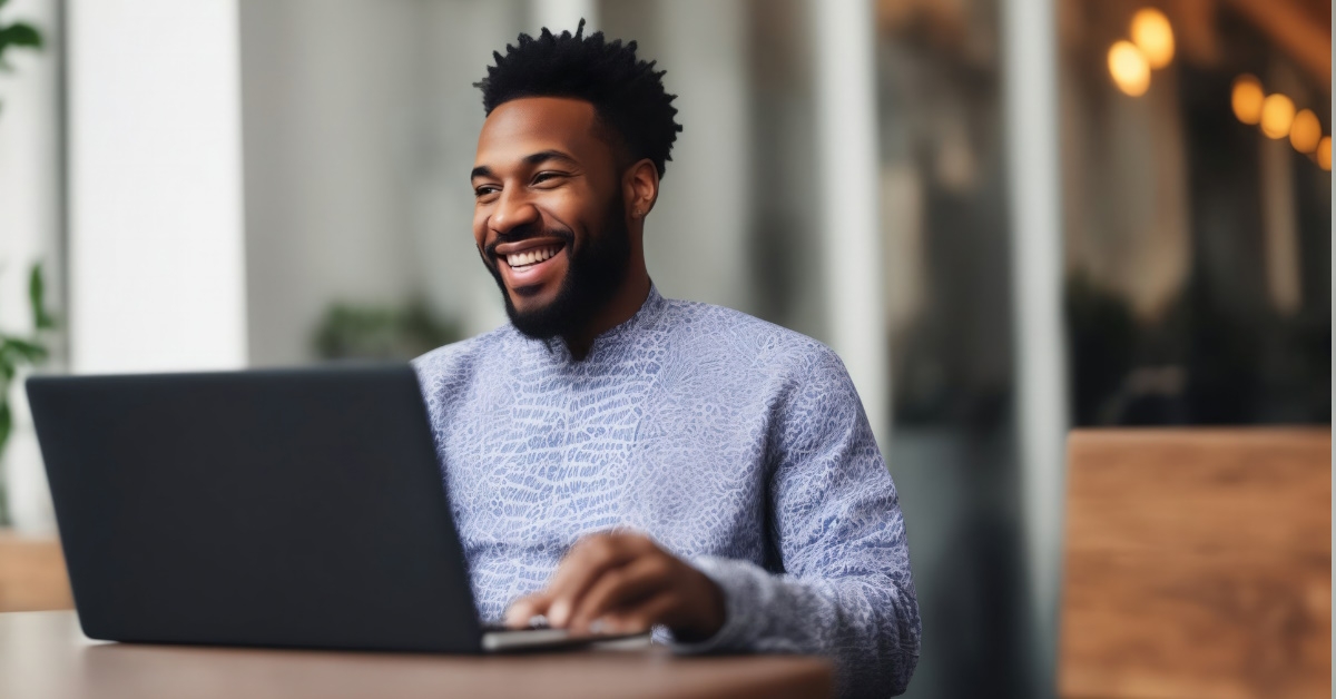 A happy African American man working on a laptop in a modern and stylish cafe located in a hotel lobby.