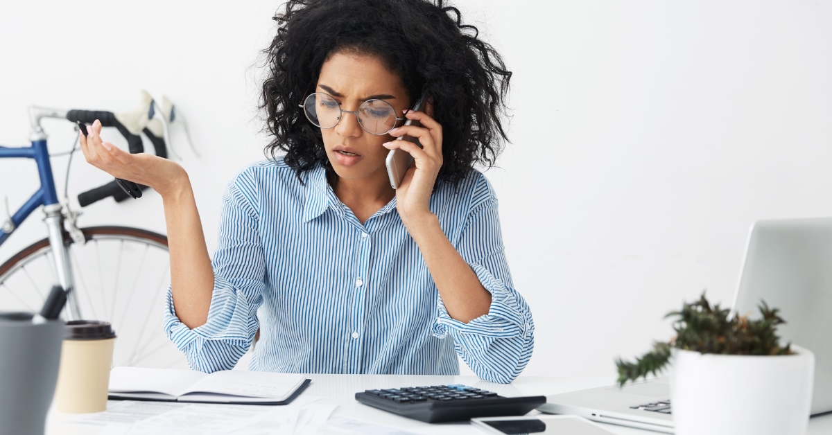 A mixed-race businesswoman having a stressful phone conversation while calling customer service to address an invoice problem.
