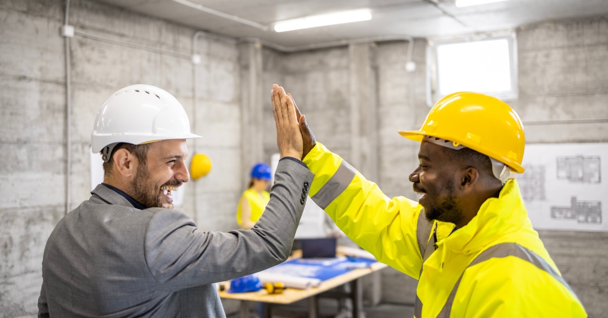 A construction worker and a structural engineer are giving a high five to each other to celebrate the successful completion of a building project.