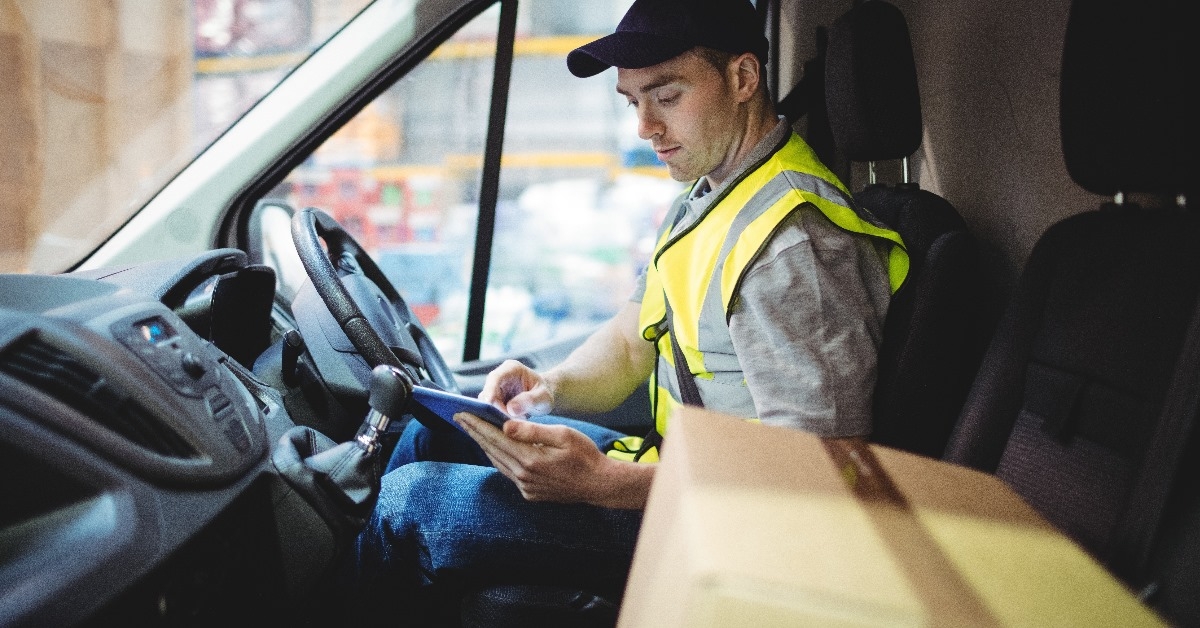 delivery driver using tablet in van with parcels on seat